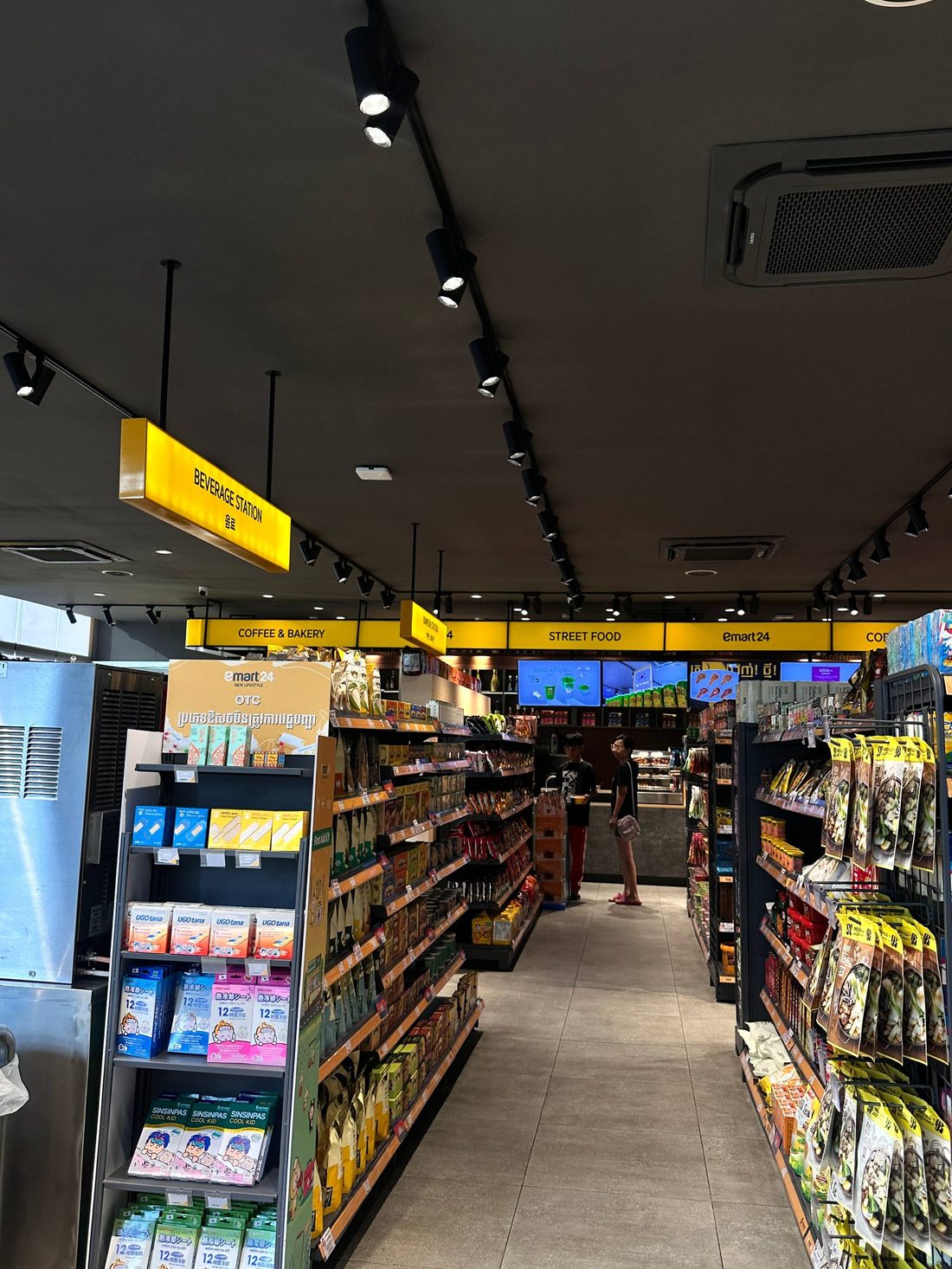 Store aisle at night with lit yellow signs reading Beverage Station, Coffee and Bakery, Street Food